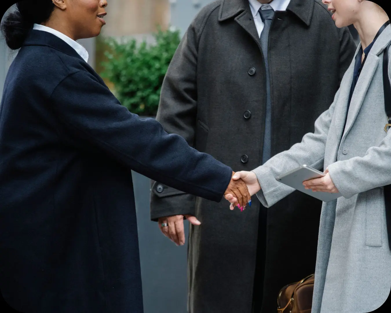 Crop anonymous diverse businesswomen in trendy elegant coats shaking hands after important conference on street